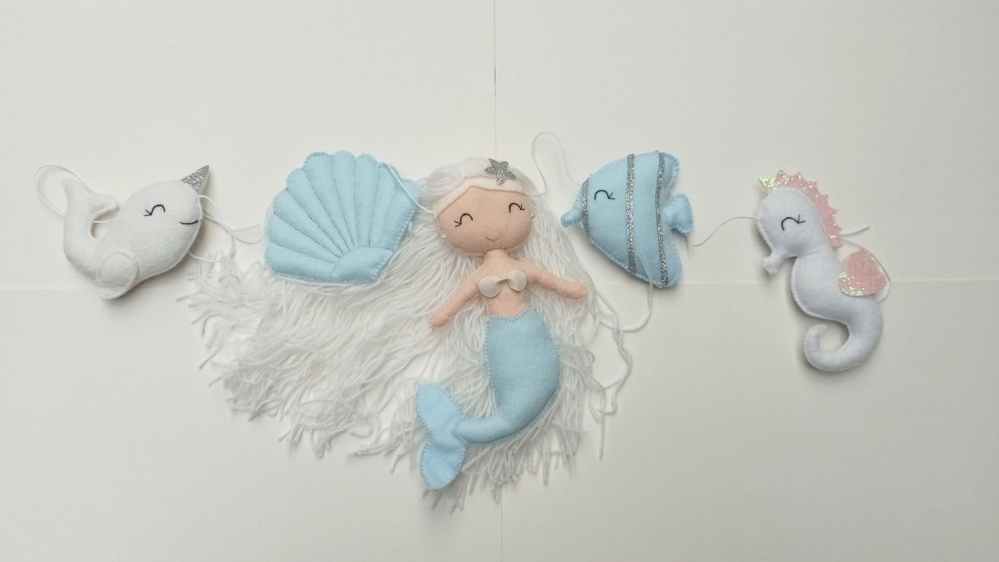 Guirlande décorative sur le thème océan composé d'une sirène, d'un hippocampe, d'un narval, d'un poisson et d'un coquillage. Couleur bleu ciel, blanc et argent.
