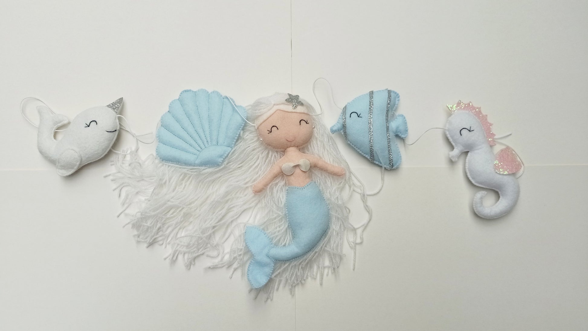 Guirlande décorative sur le thème océan composé d'une sirène, d'un hippocampe, d'un narval, d'un poisson et d'un coquillage. Couleur bleu ciel, blanc et argent.