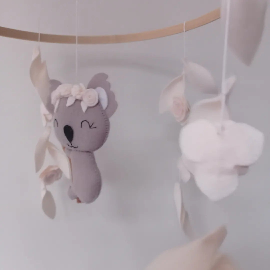 Koala gris en feutrine fait main avec tête ornée d'une couronne de fleurs blanches.