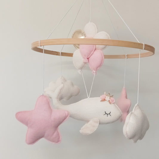 Mobile décoratif pour chambre de bébé fille composé d'une baleine blanche, d'étoiles roses, de nuages blancs et de ballons roses, blancs et dorés.