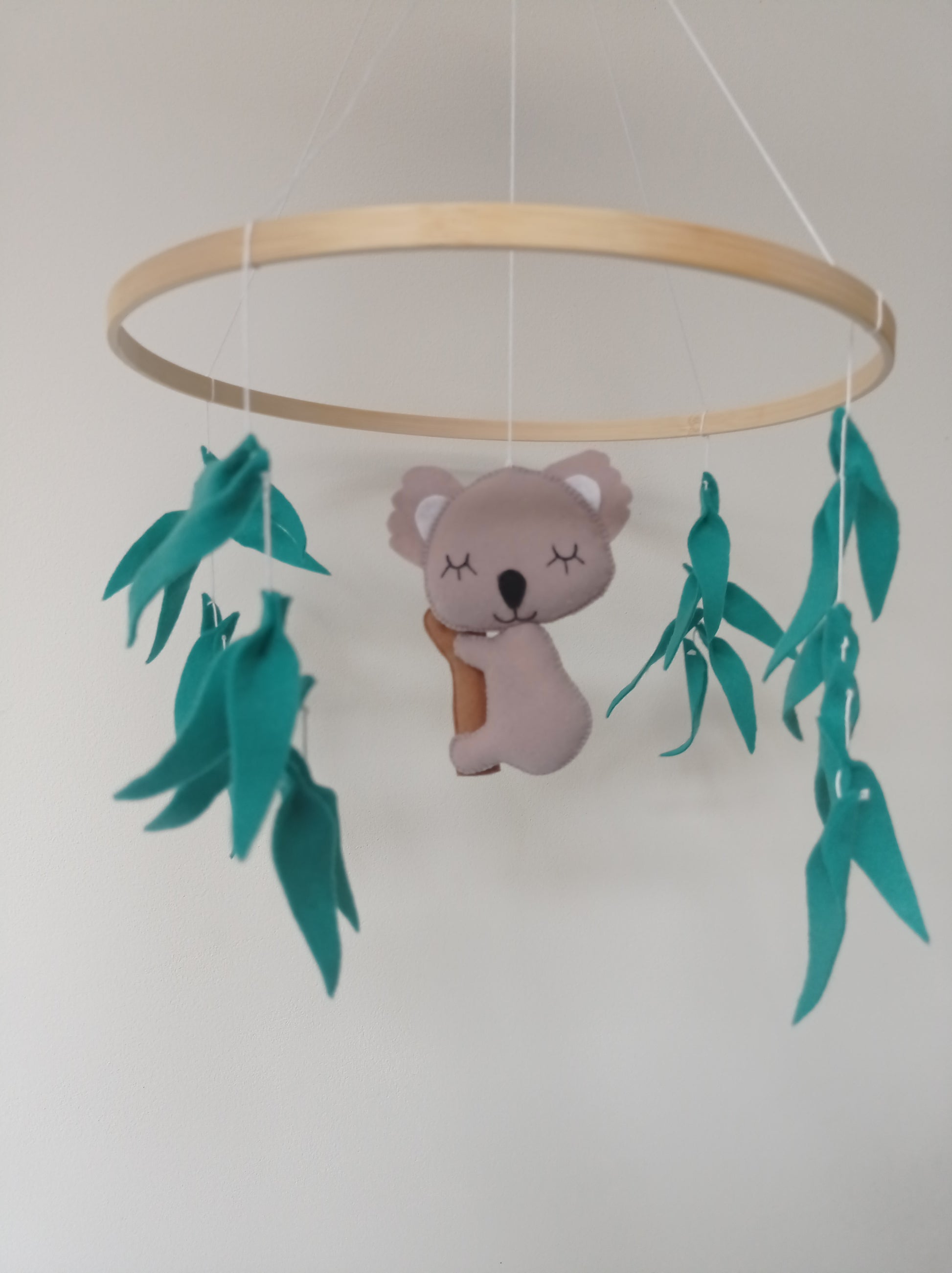 Mobile pour bébé composé d'un koala en feutrine et de feuilles d'eucalyptus vertes.