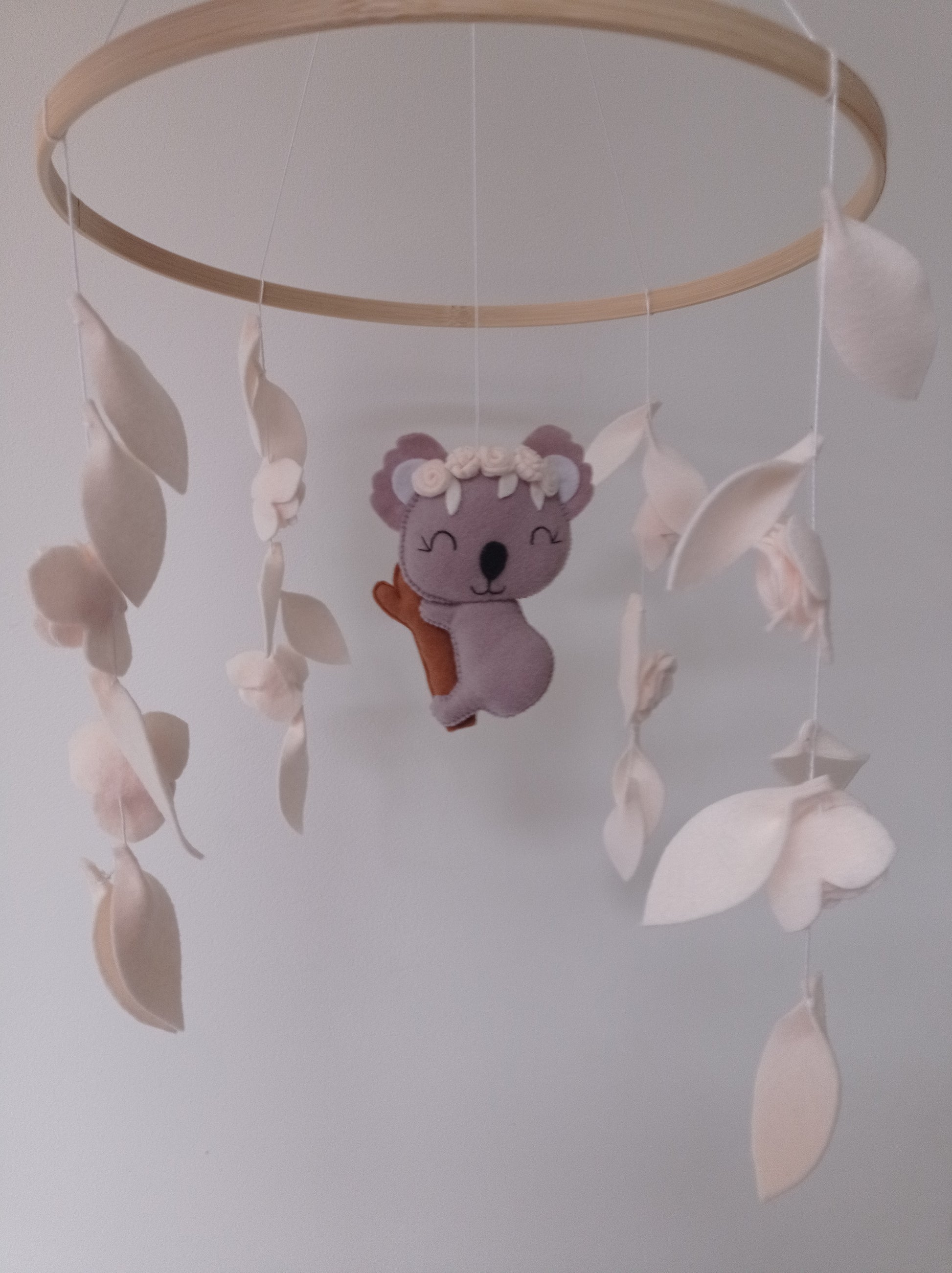 Mobile pour bébé composé d'un koala en feutrine et de feuilles et de fleurs en feutrine blanche.